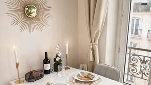 A dining table set with candles, plates, and a bottle, with a decorative sunburst wall art and a view of buildings through a window. - 1565 Pétion (Paris)