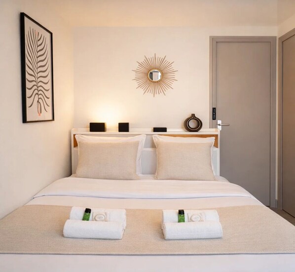 A hotel room with a bed, two bedside tables, a wall-mounted mirror, a framed artwork, and a door.
