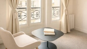 A room with a window, a chair, a table, and a radiator. - 1565 Pétion (Paris)