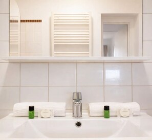 A bathroom with a white sink, two white towels, two bottles of lotion, a mirror, and a towel rack.