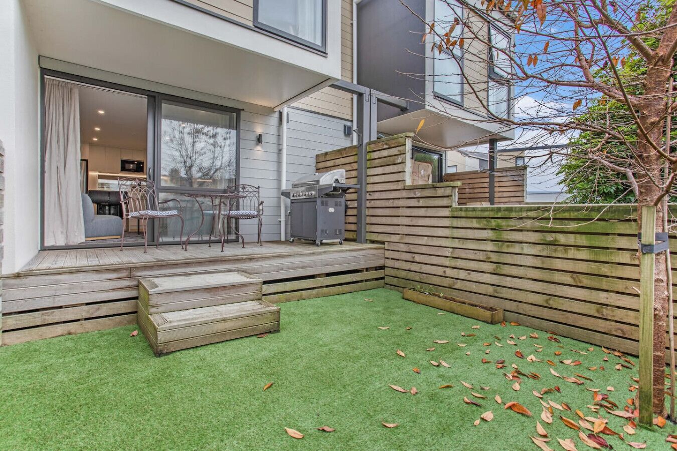 A modern outdoor patio with a wooden deck, a green artificial turf area, and a wooden fence.