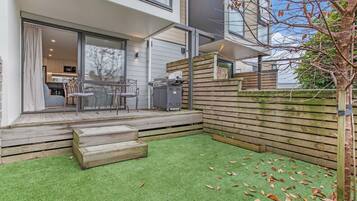 A modern outdoor patio with a wooden deck, a green artificial turf area, and a wooden fence.