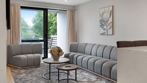 Un salon moderne avec un canapé gris, deux fauteuils, une petite table ronde et un vase de fleurs.