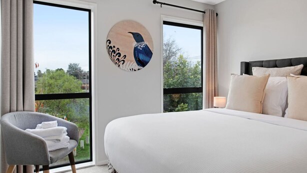 Une chambre avec un grand lit, une chaise, une fenêtre et un élément décoratif mural.
