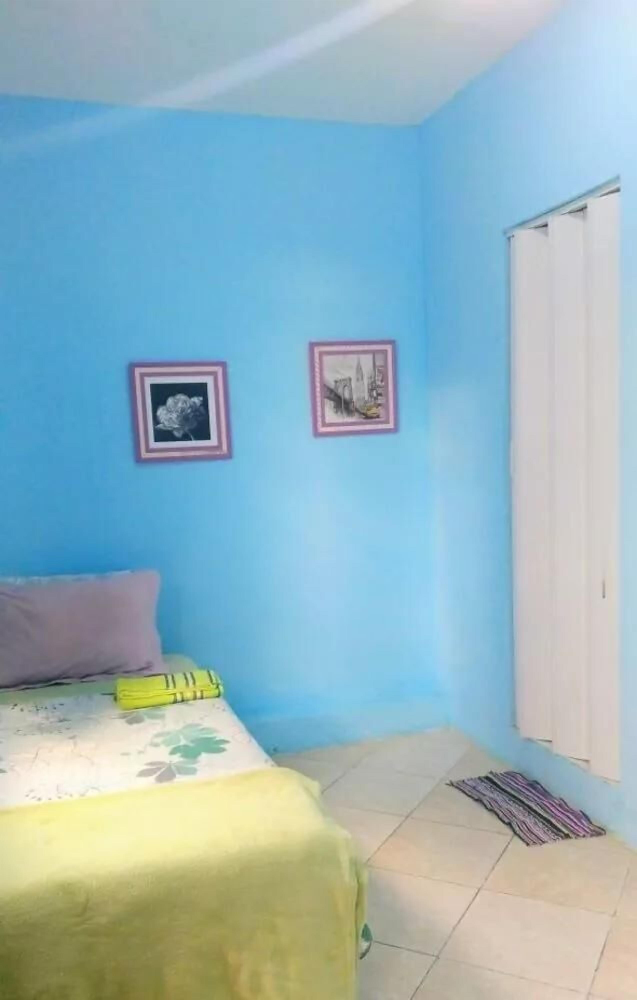 A room with a bed, a window with blinds, and two framed pictures on the wall.