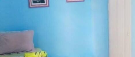 A room with a bed, a window with blinds, and two framed pictures on the wall.