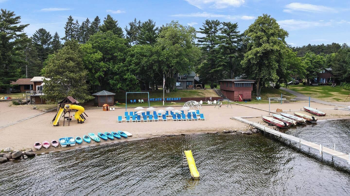Un resort junto al lago con playa de arena, área de juegos para niños y muelle con barcos.