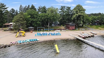 Un resort junto al lago con playa de arena, área de juegos para niños y muelle con barcos.