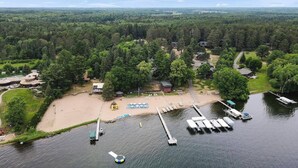 An aerial view of a lakeside property with a sandy beach, docked boats, and a cabin labeled "HEATH BERRY."