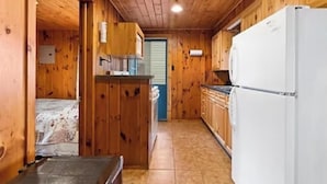 A compact kitchen with wooden walls and a tiled floor, featuring a refrigerator, cabinets, and a sink.