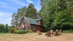 A rustic wooden house with a green roof, surrounded by a dry grassy yard and a few wooden chairs. - Cabin 9 in Heath's Resort (Pine River)