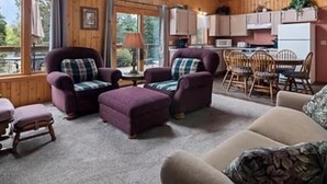 A cozy cabin interior with wooden walls, a large window, a dining area, and a kitchen. - Cabin 9 in Heath's Resort (Pine River)