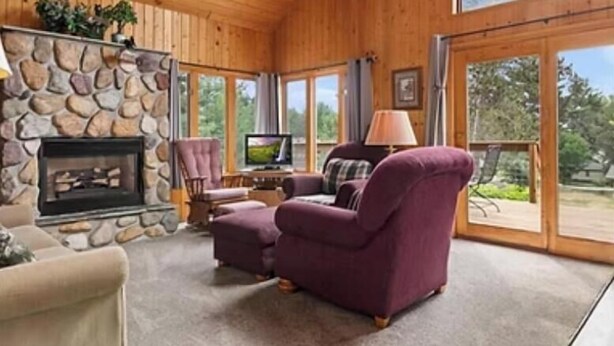 A cozy living room with a stone fireplace, large windows, and comfortable seating. - Cabin 9 in Heath's Resort (Pine River)
