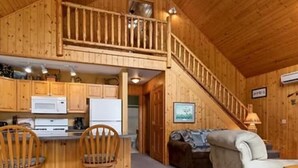 A wooden cabin interior with a kitchen, dining area, and living room.