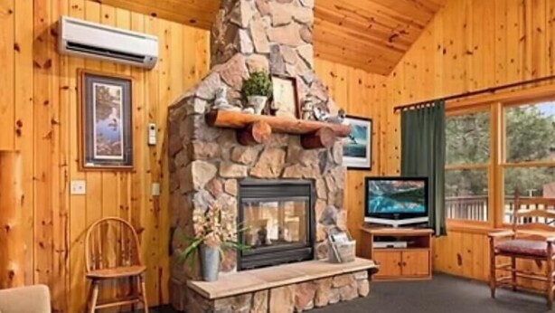 A cozy cabin interior with a stone fireplace, wooden walls, a television, and a comfortable seating area. - Cabin 12 at Heath's Resort (Pine River)