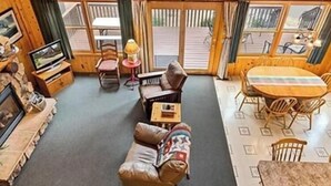 A cozy cabin interior with a wooden ceiling, a sofa, a TV, a dining table, and a fireplace. - Cabin 12 at Heath's Resort (Pine River)