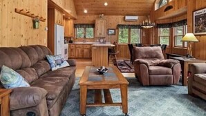 Interior rústico de una cabaña con techo de madera, una cabeza de venado montada, una zona de cocina y un rincón de estar acogedor.