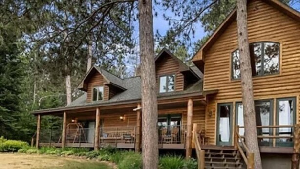 A log cabin with a porch, a covered deck, and a staircase leading to the main entrance.