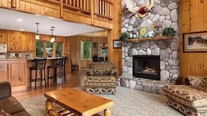 A spacious lodge with a stone fireplace, wooden furniture, and a high ceiling.