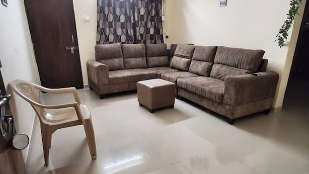 A living room with a brown sofa, a small wooden chair, and a matching ottoman. - 1BHK Cozy Stay 2 (Pune)