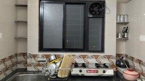 A kitchen with a gas stove, a sink, and a window with a fan. - 1BHK Cozy Stay 2 (Pune)
