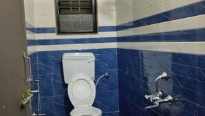 A bathroom with a toilet, a shower, and a window with a metal grate. - 1BHK Cozy Stay 2 (Pune)