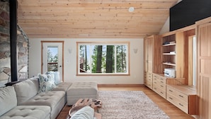 A cozy living room with a stone wall, a large window, a wooden ceiling, and a built-in wooden cabinet.