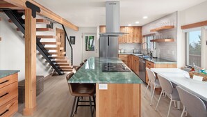A modern kitchen with a central island, wooden staircase, and built-in cabinets.