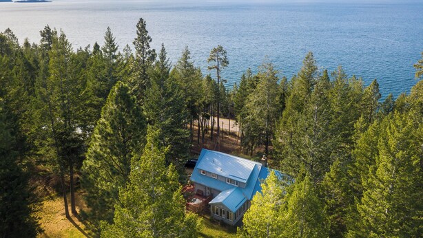 A house surrounded by dense forest with a view of a large body of water and distant mountains.
