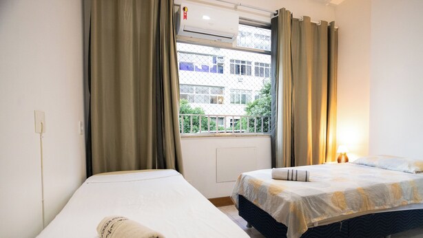 Ein Hotelzimmer mit zwei Betten, einem Fenster mit Vorhängen, einer Klimaanlage und einer Lampe.