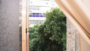 Blick von einem Balkon mit einer Kachelwand und einem Metallgeländer. Im Hintergrund ein Gebäude mit mehreren Fenstern und ein Baum.