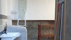 A compact, well-lit room with a wooden floor, a white sink, a striped chair, a drying rack, and a broom leaning against the wall.