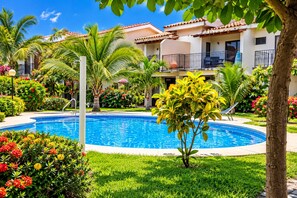 A swimming pool surrounded by lush greenery and a building with balconies.