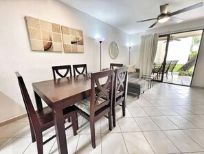 Un área de comedor con una mesa y sillas de madera, un ventilador de techo y vistas al exterior a través de un ventanal.