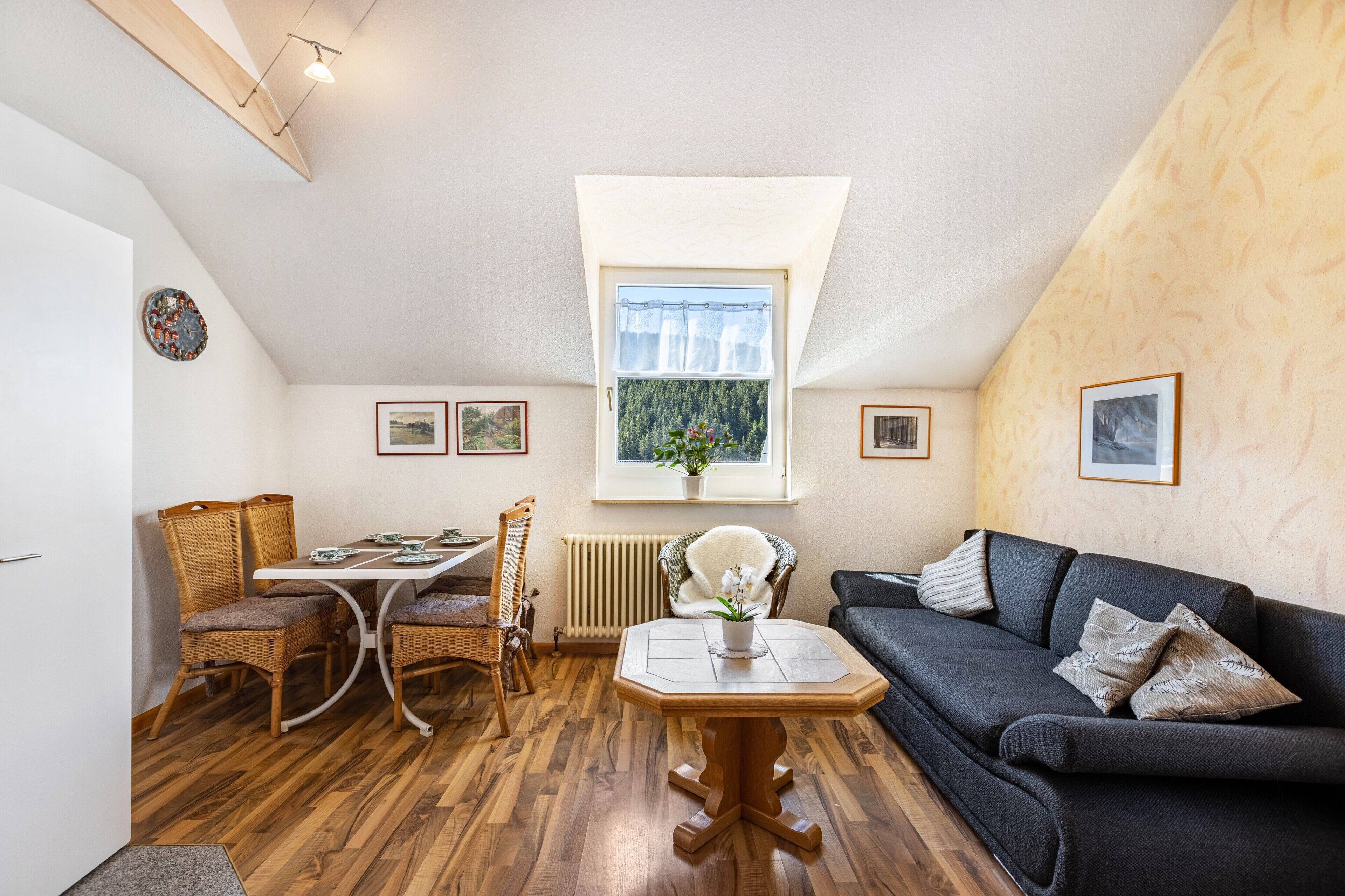 Une pièce chaleureuse avec une table à manger, des chaises, un canapé, une fenêtre donnant sur un beau paysage et des tableaux encadrés accrochés aux murs.