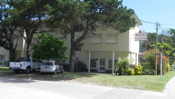 A two-story building with a sign that reads "HOTEL SAN REMO". There are two parked cars in front of the building. - Hotel San Remo (Pinamar)