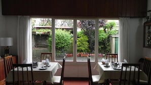 A dining area with two tables and chairs, a window with a view of a garden. - Hotel San Remo (Pinamar)