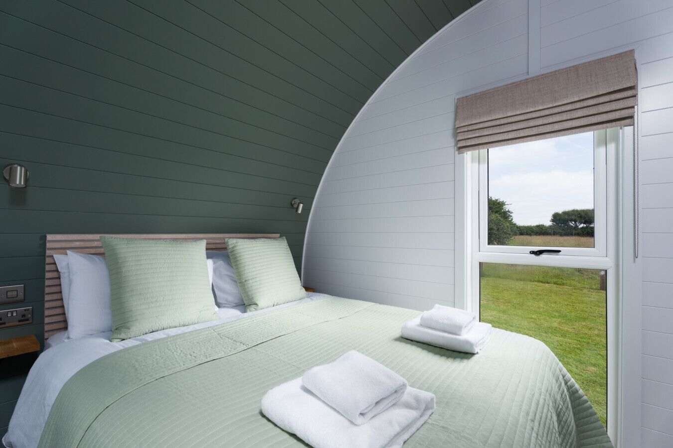 Ein Schlafzimmer mit gewölbter Decke, einem Bett mit grüner Bettwäsche, einem Fenster mit Blick ins Freie und einem Nachttisch mit Lampe.