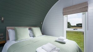Une chambre à coucher avec un plafond incurvé, un lit avec une literie verte, une fenêtre donnant sur l’extérieur et une table de chevet avec une lampe.