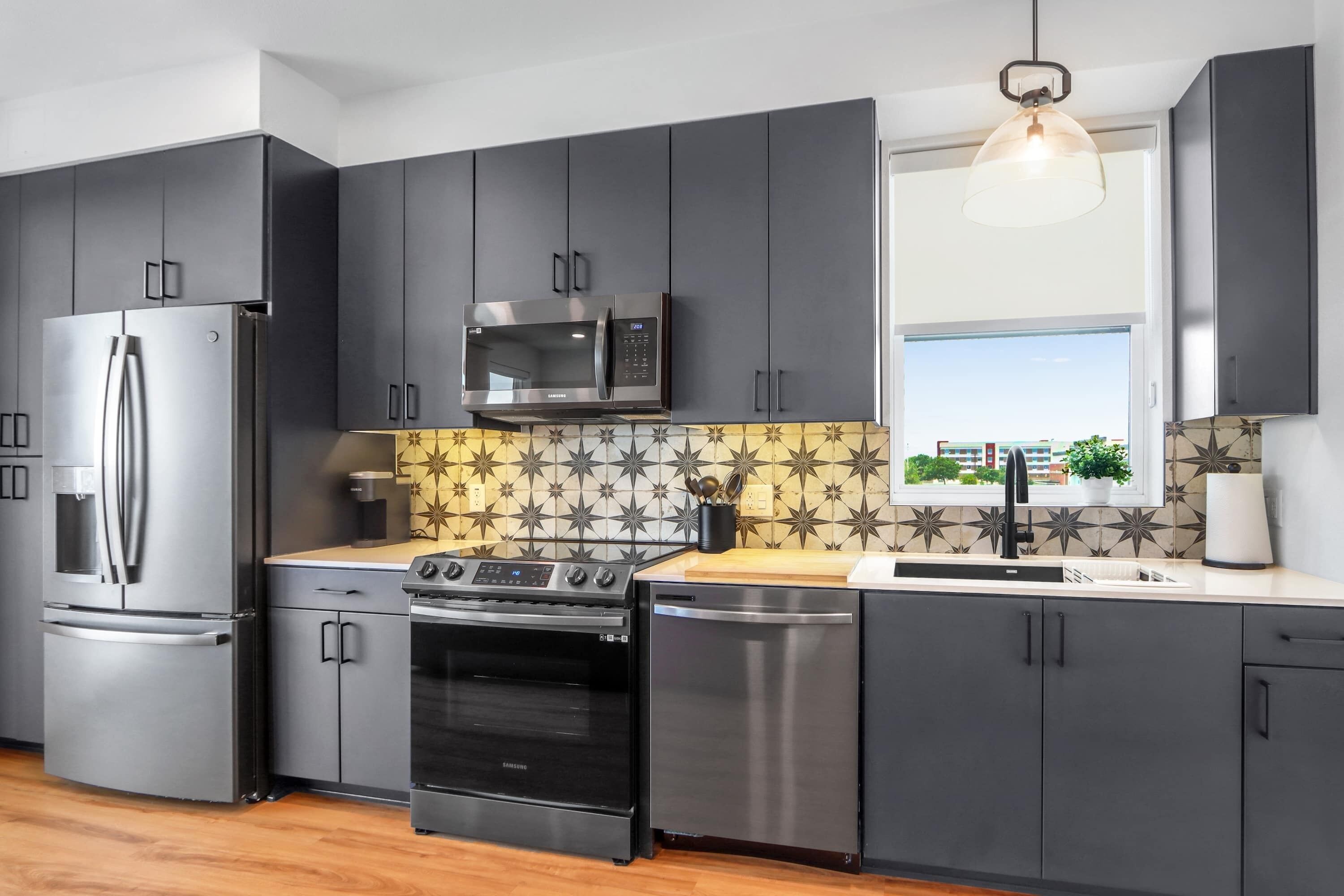 A modern kitchen with dark cabinets, stainless steel appliances, a microwave, oven, and dishwasher.
