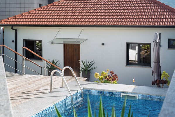 Ett modernt hus med en swimmingpool, en trädörr och ett tak täckt med takpannor.