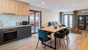 A modern kitchen with built-in appliances, a dining area with a wooden table and chairs, and a seating area with a sofa and curtains.