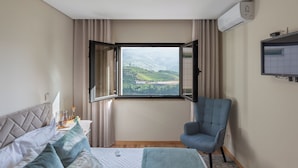 A hotel room with a bed, a chair, a window with curtains, and an air conditioning unit.