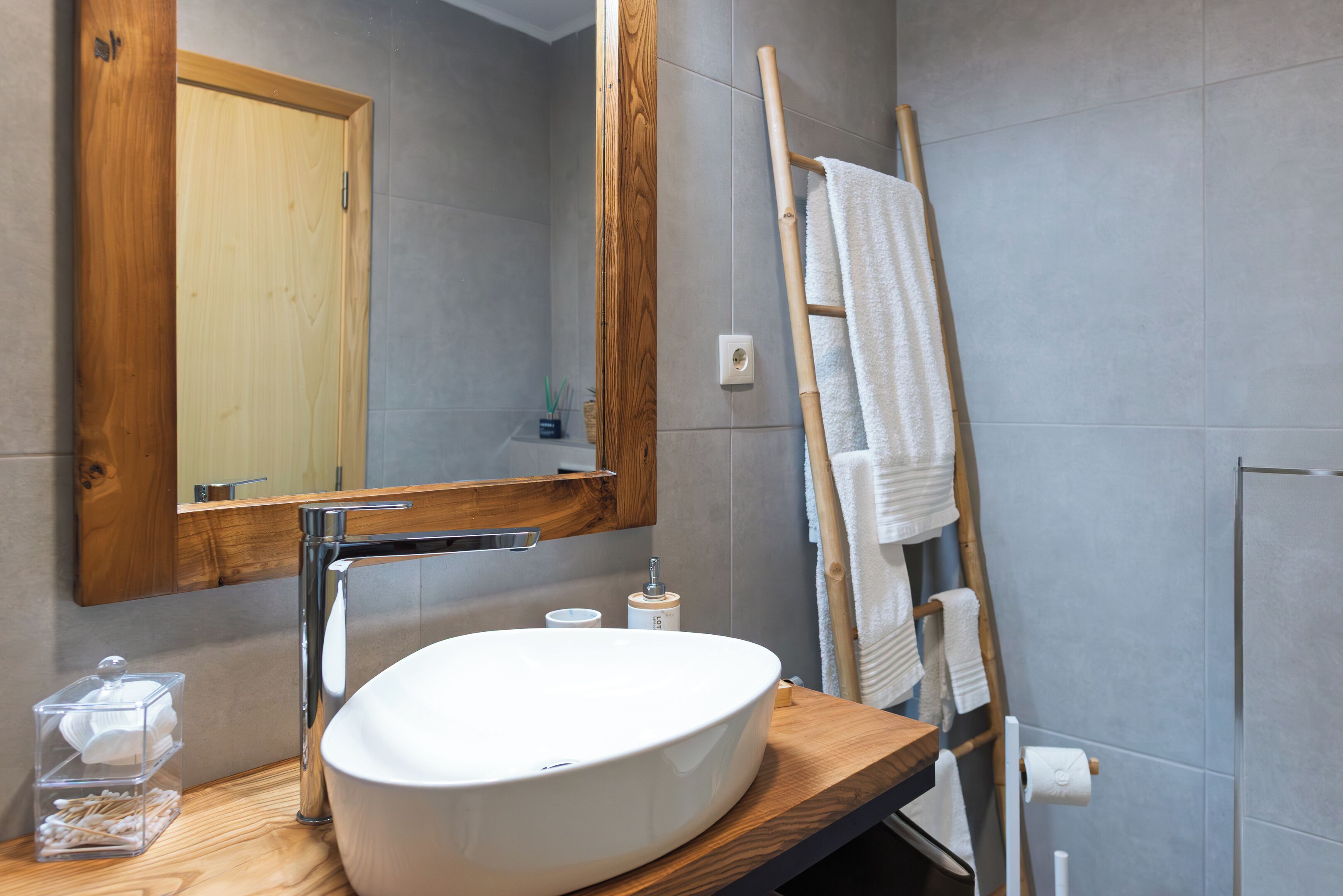 Un bagno moderno con un mobile bagno in legno, uno specchio grande, un lavandino bianco e un porta asciugamani.
