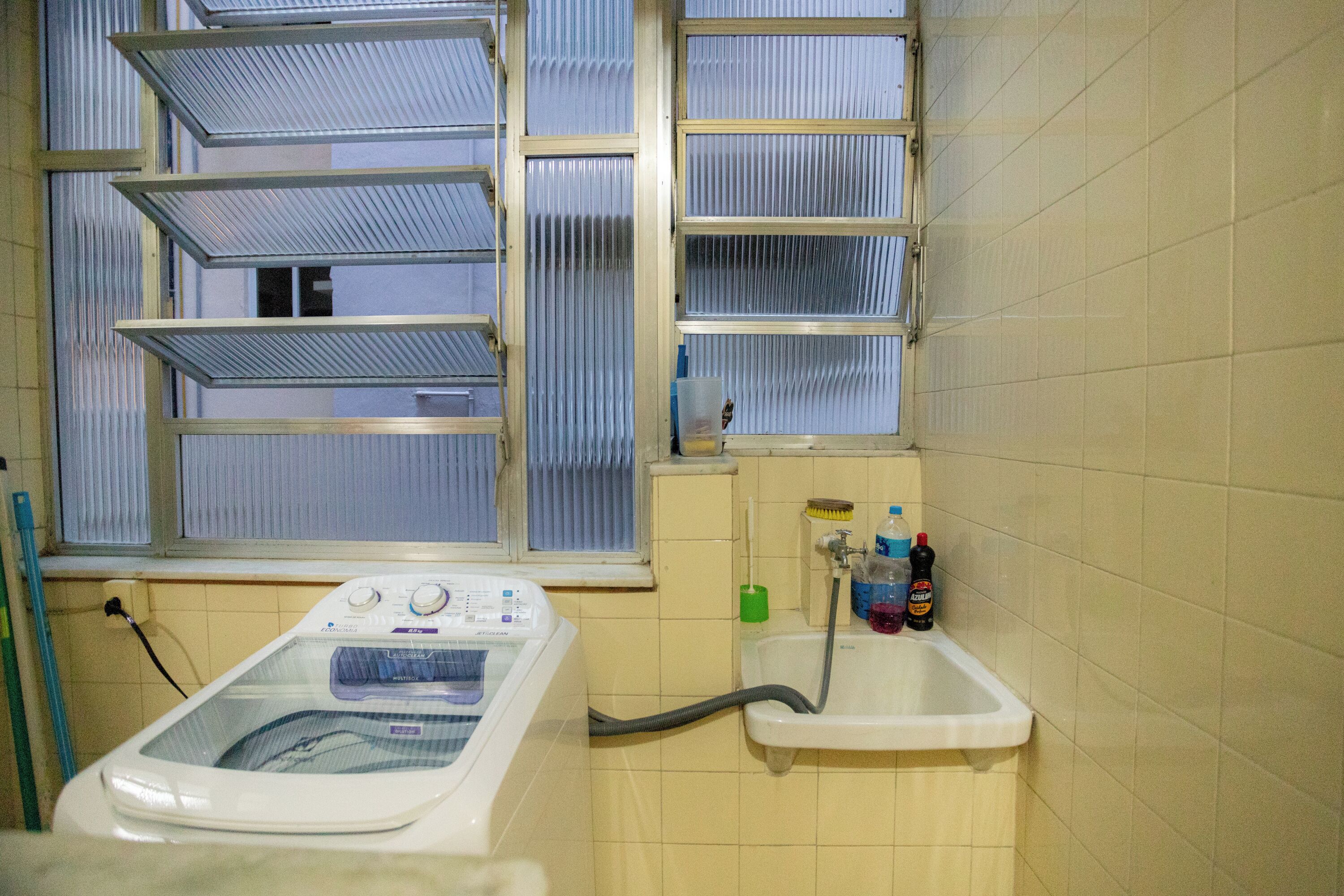 A laundry area with a washing machine, a sink, and a window with blinds.