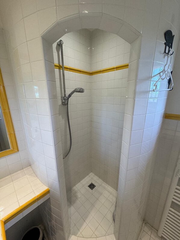 A small, enclosed shower area with white tiles and a yellow accent strip.