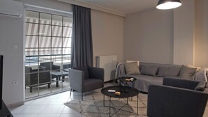 A modern living room with a sofa, armchairs, a coffee table, and a balcony with outdoor furniture.