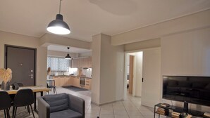 A modern living room with a sofa, coffee table, TV, and a dining area with chairs and a table.