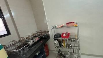 Una cocina con un estante metálico que contiene ollas y sartenes, una cesta metálica y un recipiente rojo.