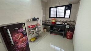 A compact kitchen with a refrigerator, stove, and various kitchen utensils. - 1 bhk comfy stay 1 (Pune)